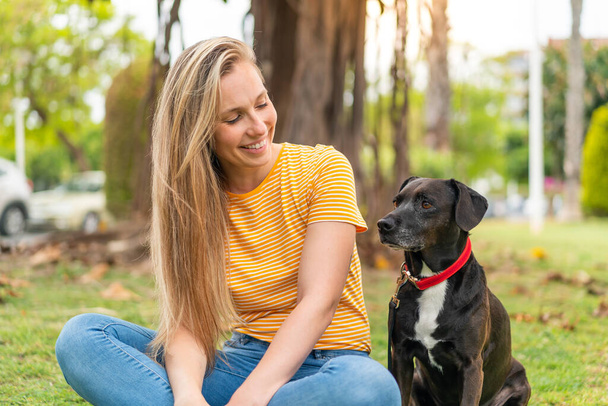 Dışarıda sevimli siyah köpeği olan genç sarışın kadın. - Fotoğraf, Görsel
