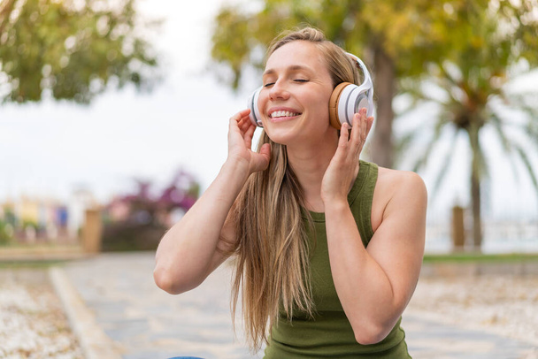 Açık havada müzik dinleyen genç sarışın kadın. - Fotoğraf, Görsel