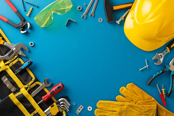 Labor Day theme. Top view of worker's equipment, tool belt, hard hat, safety glasses, construction gloves, dowel nails, pliers, screwdriver, hammer, blue backdrop, empty space for appreciation message - Photo, Image