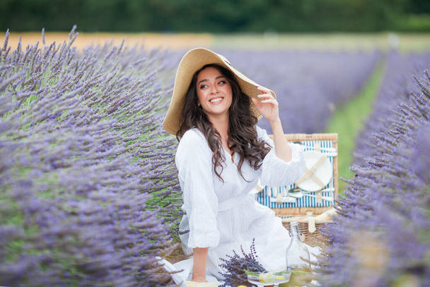 Campo de lavanda. Hermosa mujer rizada de pelo oscuro en vestido simple blanco en el campo de flores púrpuras. - Foto, imagen