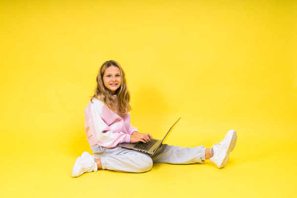 Pozitív gyerek ül egy laptop olvasni házi feladatot viseljen alkalmi stílusú ruhát elszigetelt sárga háttér - Fotó, kép