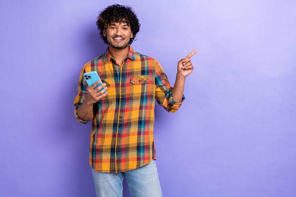 Photo of young blogger guy wear checkered shirt direct finger empty space information spotify web app isolated on violet color background. - Φωτογραφία, εικόνα