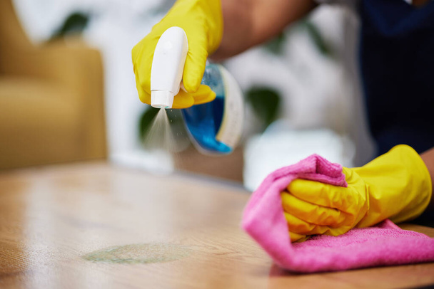 Spray, kéz és személy tisztító asztal, bútorok és takarítási szolgáltatások otthon. Tisztább törlőkendő felület közelsége ronggyal, vegyipari termékkel és por, baktériumok és szennyeződések fertőtlenítésével. - Fotó, kép
