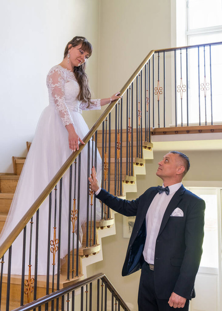 La sposa è in piedi sulle scale, a guardare lo sposo. E 'di sotto. nozze, amore - Foto, immagini