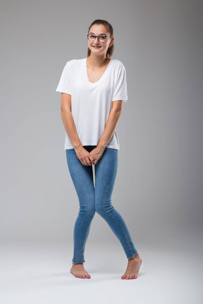 žena se svázanými vlasy, oblečená v bílé košili a hubených džínách, zkříží nohy, snaží se odvrátit naléhavou potřebu močit - Fotografie, Obrázek