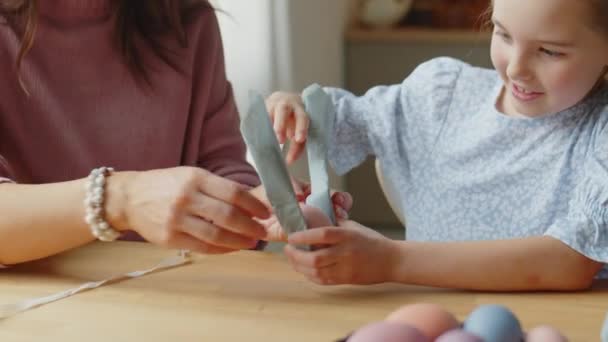 Plan incliné de la petite fille décorant oeuf de Pâques avec l'aide de la mère tout en se préparant pour les vacances à la maison - Séquence, vidéo