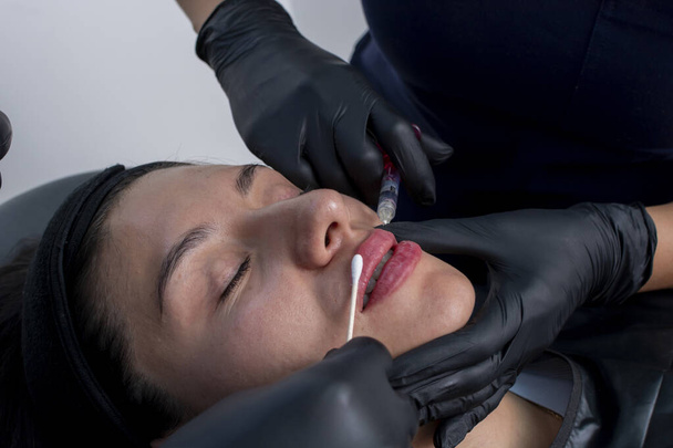Közelkép egy fiatal nő arcáról, akit hialuronsavval injekcióznak, hogy feldagassza az ajkait. - Fotó, kép