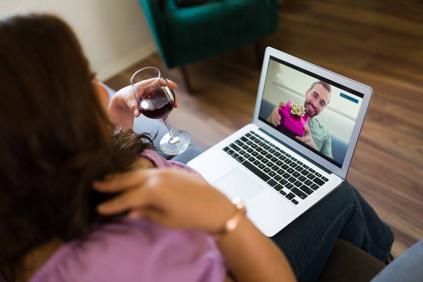 オンライン技術を使用してワインと花とのロマンチックなビデオ通話を持つカップルのバーチャルデートのリアビュー - 写真・画像
