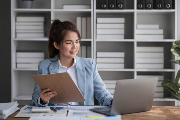 Веселая деловая леди, работающая на ноутбуке в офисе, азиатка счастливая красивая деловая женщина в формальном костюме работает на рабочем месте. Привлекательная улыбка сотрудницы офиса. - Фото, изображение