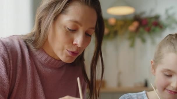 Κοντινό πλάνο της μητέρας που μιλάει με την κόρη του ενώ ζωγραφίζει μαζί πασχαλινά αυγά κατά τη διάρκεια των διακοπών στο σπίτι - Πλάνα, βίντεο