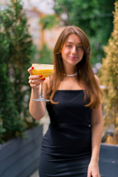Egy fiatal, mosolygós lány portréja koktéllal a kezében, aki egy nyári teraszon áll egy bárban. - Fotó, kép