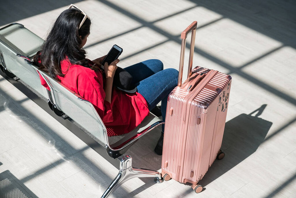 Hátsó ázsiai nő ülni várakozó ülések és játszani smartphone vagy mobiltelefon világos árnyalatú a repülőtér indulási terminál. - Fotó, kép