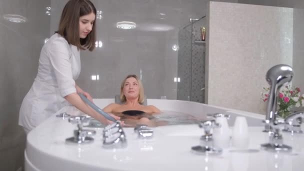 Health massage with a jet of water for a young beautiful blonde. Hydro procedures in the spa salon. Massage. A woman in a hot tub - Záběry, video