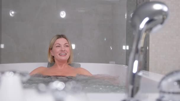 Portrait of a smiling blonde woman taking a hot bath with warm bubbles. Health procedures in the spa salon. - Séquence, vidéo