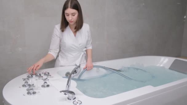 A young spa cosmetologist girl adjusts the hydrobath before the procedure. Hydromassage bath in the salon. Correct water temperature. - Filmati, video
