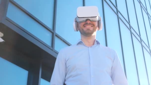 Офисный работник использует очки виртуальной реальности, стоя рядом со стеклянным бизнес-центром. Виртуальные технологии в бизнесе. Вертикальное видео - Кадры, видео