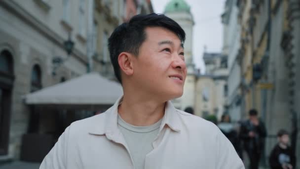 mężczyzna portret szczęśliwy uśmiechnięty zamyślony natchniony azjatycki mężczyzna turysta rozglądając się na zewnątrz marząc chiński facet korzystając Cityscape zwiedzanie stojąc w centrum miasta sen badania architektury - Materiał filmowy, wideo