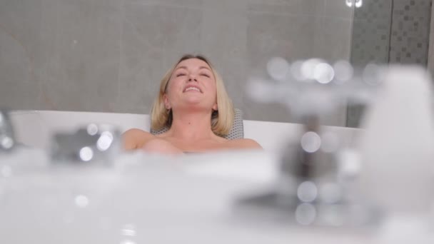 Portrait of charming woman sitting relaxed in hydromassage bathtub in luxury spa salon, smiling. Happy woman lying in bathtub, relaxing hydrotherapy in beauty center. - Metraje, vídeo