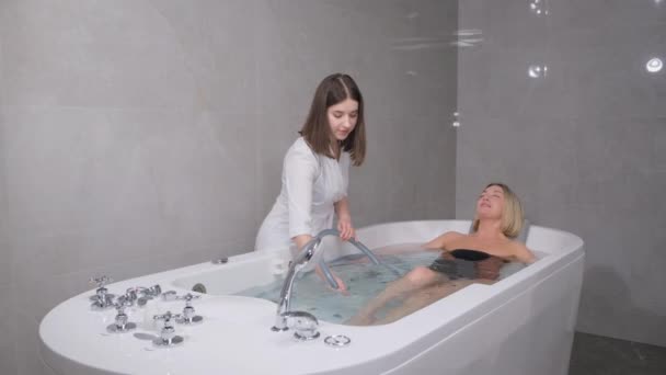 A young cosmetologist gives a beautiful blonde a soothing and rejuvenating water massage. Procedures in the spa salon. Vacation. Caring for your own body. - Záběry, video