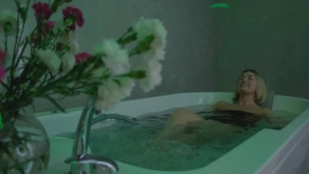 Happy woman lying in bathtub, relaxing hydrotherapy in beauty center. A luxurious woman enjoys a hot tub in a luxury spa - Imágenes, Vídeo