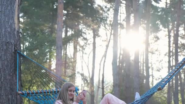 A woman with a phone in a hammock. Relaxing in the countryside during the summer holidays. - Séquence, vidéo