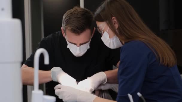 Un dentista y su asistente durante el tratamiento dental utilizando métodos de tratamiento modernos. Tratamiento oportuno de enfermedades de la cavidad oral - Imágenes, Vídeo
