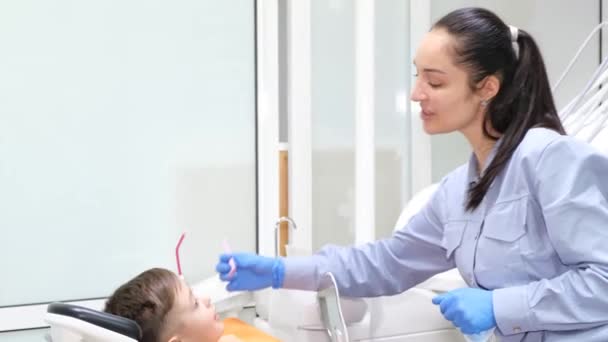 Küçük bir çocukla dişçi muayenesi sırasında genç ve çekici bir dişçi. Modern pediatrik dişçilik. - Video, Çekim