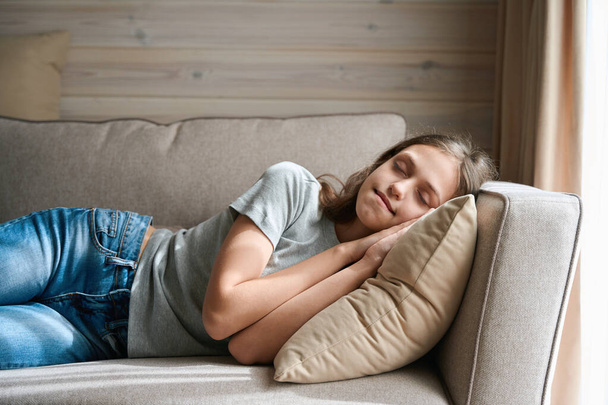 Ruhige junge Dame schläft auf gemütlicher Stoffcouch am Fenster im Wohnzimmer - Foto, Bild