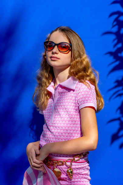 Modelo atraente Barbie menina estilo vestindo óculos de sol, tee-shirt rosa e shorts com cabelos longos no fundo azul, conceito de moda vintage. Foto de alta qualidade. - Foto, Imagem