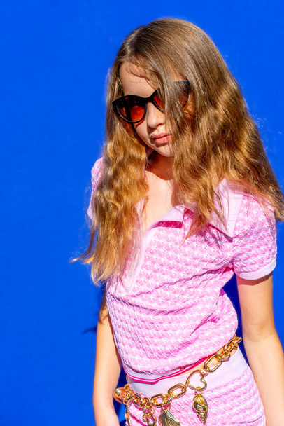 Modèle attrayant Barbie fille de style portant des lunettes de soleil, un tee-shirt rose et un short avec des cheveux longs sur fond bleu, concept de mode vintage. Photo de haute qualité. - Photo, image