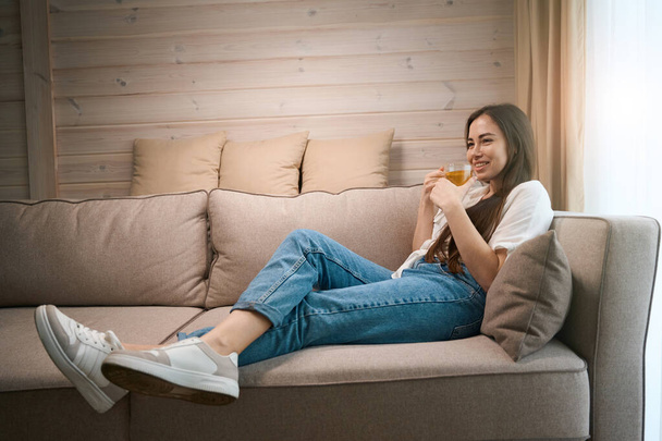 Portrét šťastné dámy relaxační pití šálek horkého čaje a těší klidný čas a vnitřní prostředí v útulném domě - Fotografie, Obrázek