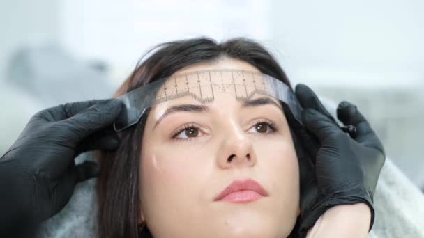 A cosmetologist performs a permanent eyebrow make-up procedure using a special tattoo needle. A woman in a beauty salon. Eyebrow tattoo. The pigment is injected under the skin. Cosmetology - Metraje, vídeo