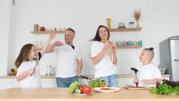 Een familie danst en zingt in de keuken tijdens het koken. Zoon en dochter hebben plezier met hun ouders - Video