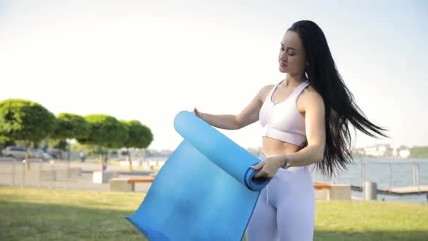 A beautiful brunette with a fitness mat in her hands for morning exercise. Sports women. Fitness concept - Záběry, video