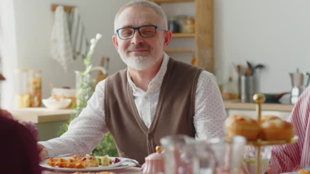 Portrét staršího muže pózujícího pro kameru na svátečním jídelním stole při oslavách Velikonoc s rodinou - Záběry, video
