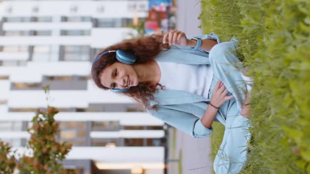Fröhlich entspannte überglückliche Frühchen in drahtlosen Kopfhörern, die beim Smartphone-Tanzen bevorzugte energiegeladene Disco-Rock 'n Roll-Musik hören. Mädchen auf Gras im städtischen Stadtpark. Vertikal - Filmmaterial, Video