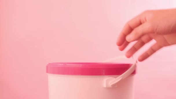 Χέρια άνοιγμα λευκό κουβά με ροζ κορυφή σε ροζ φόντο - Πλάνα, βίντεο