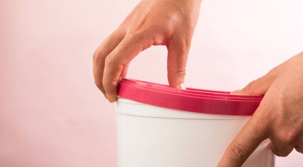 Mãos abrindo balde branco com top rosa no fundo rosa - Foto, Imagem