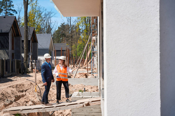 General contractor and forewoman inspecting interior of house under construction, walking along construction site and controlling compiance with safety regulations - Fotoğraf, Görsel