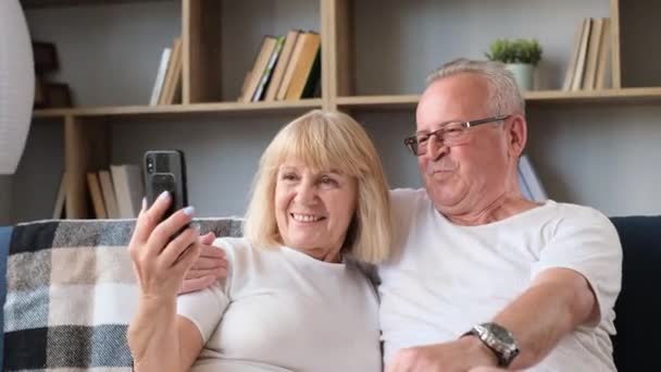 Happy senior couple taking selfie, having fun with phone camera, smiling elderly wife and husband hugging, looking at camera, posing for photo. - Materiał filmowy, wideo