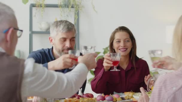 Rodzinna para i ich starsi rodzice brzęczą kieliszkami w toście, rozmawiają i uśmiechają się przy stole podczas wspólnej kolacji w domu - Materiał filmowy, wideo
