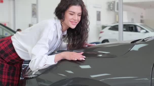 A beautiful girl strokes an electric car. Buying a new car at a dealership. - Video, Çekim