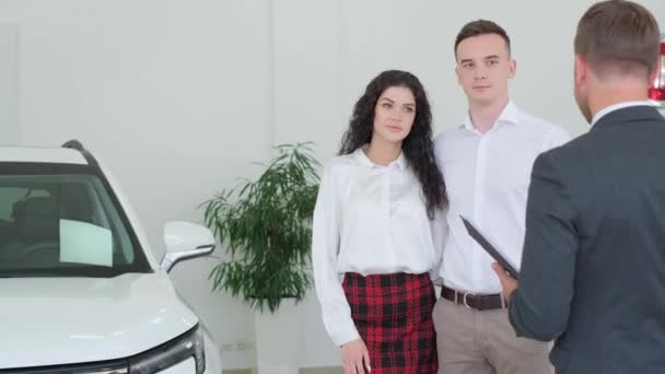 A car sales manager shows a new electric car in a car showroom. Car sales concept. - Filmati, video