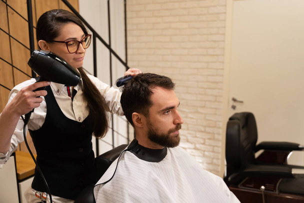 Coiffeur sèche les cheveux du client avec un sèche-cheveux professionnel, le mâle est situé dans la chaise de coiffure - Photo, image