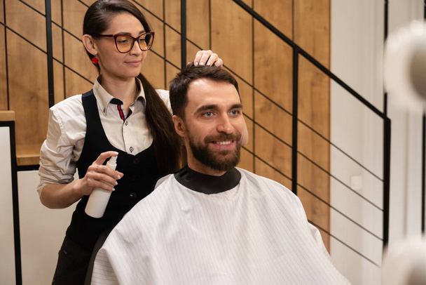 Parrucchiere in barbiere si prende cura dei capelli di un maschio, il cliente si trova in una comoda sedia - Foto, immagini