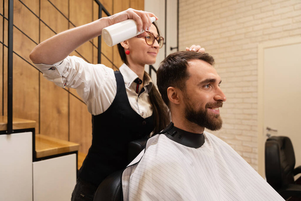 Artigiana in un barbiere si prende cura di un capello maschile, il cliente è seduto su una comoda sedia - Foto, immagini