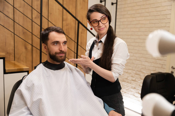 Parturi naaras työskentelee asiakkaan kanssa modernissa parturissa, työssään hän käyttää hiusmuotoilutuotetta - Valokuva, kuva