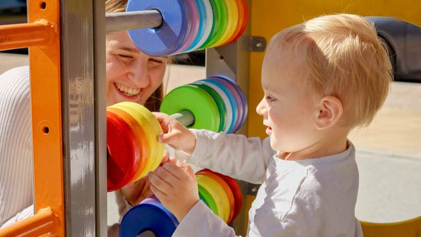 Nuori äiti opettaa hänen poikansa käyttäen värikäs helmitaulu leikkikentällä. Lapset kehitys, lasten koulutus, vauvan oppiminen - Valokuva, kuva