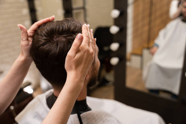 Artigiana in un barbiere fa un'acconciatura maschile, il cliente si trova di fronte allo specchio - Foto, immagini