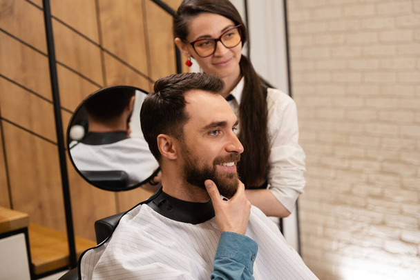 Barbiere donna dimostra la sua acconciatura dalla schiena al cliente allo specchio, il cliente sorride - Foto, immagini